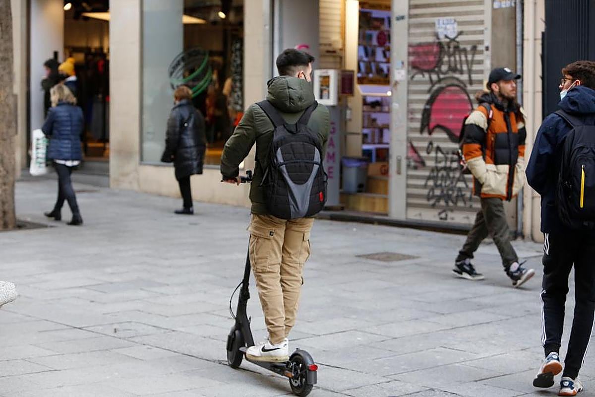 Un joven circula con su patinete por una calle peatonal de la ciudad.
