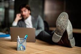 Un hombre trabaja con un ordenador y con los pies sobre la mesa.