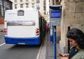 Una usuaria de autobús consulta el móvil junto al panel informativo en la parada de los soportales de San Antonio.