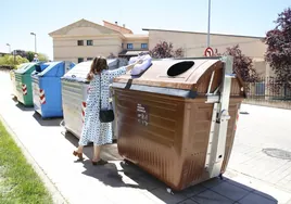 Una mujer deposita una bolsa con residuos orgánicos en un contenedor marrón.