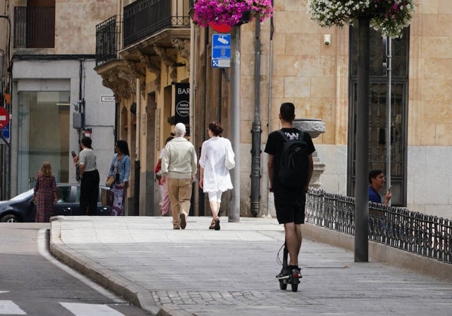 Un joven circula con un patinete por la acera de la calle San Pablo.