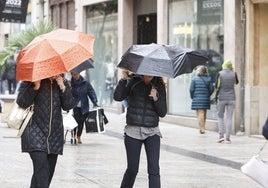 Dos salmantinas se refugian de la lluvia mientras caminan por el centro de la ciudad.