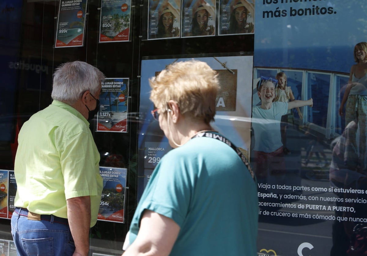 Varios mayores observan carteles de agencias de viajes.