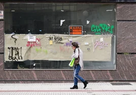 Una mujer pasa ante un local comercial cerrado.