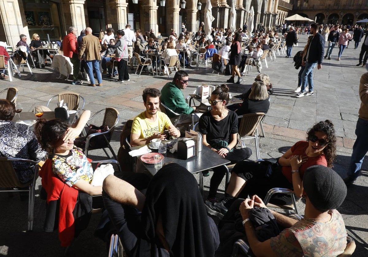 Varios jóvenes aprovechan el calor en una terraza en manga corta y se protegen del sol.