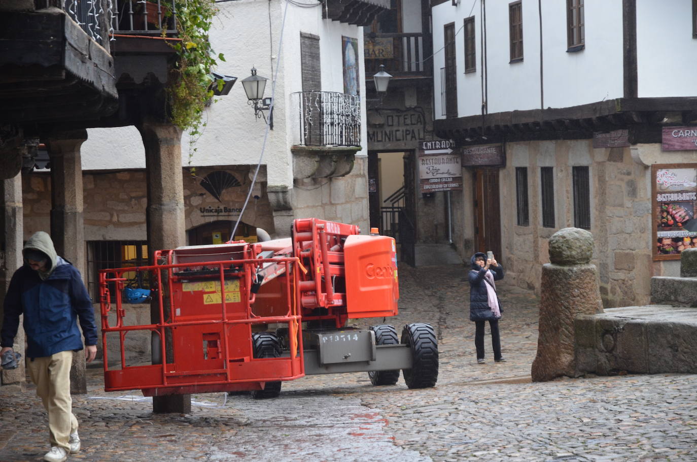 Una mujer fotografía el montaje de luces en la Plaza Mayor de La Alberca, con maquinaria y furgones.