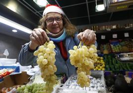 Nati Rodríguez sujeta dos racimos de uvas para Nochevieja en su puesto de frutas en el mercado.