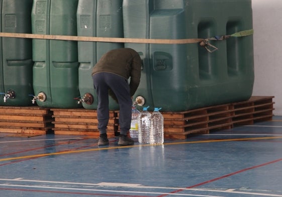 Un vecinos cogiendo agua en los depósitos instalados en el frontón cubierto.