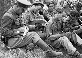 El brigadista yugoeslavo Vladimir Copic junto con miembros del Batallón británico miran unos abanicos, durante un mitin cerca del frente. Ulldemolins, Tarragona, mayo de 1938