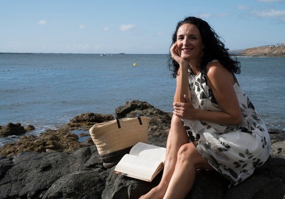 La periodista Ana Salamanca junto a la playa con un libro.