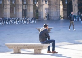 Un hombre sentado en un banco de la Plaza Mayor en un día soleado de frío.