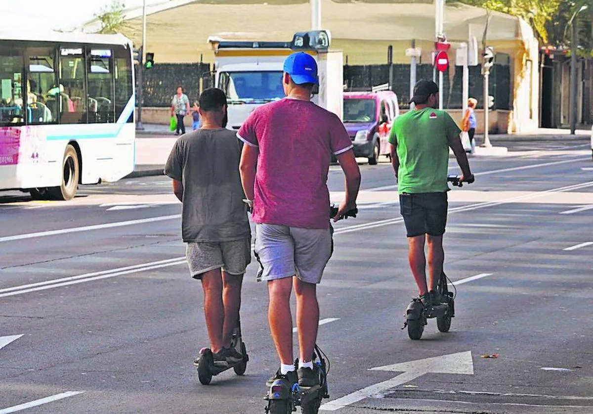 Tres hombres circulan en paralelo y sin cascos con patinetes eléctricos por la avenida de María Auxiliadora.