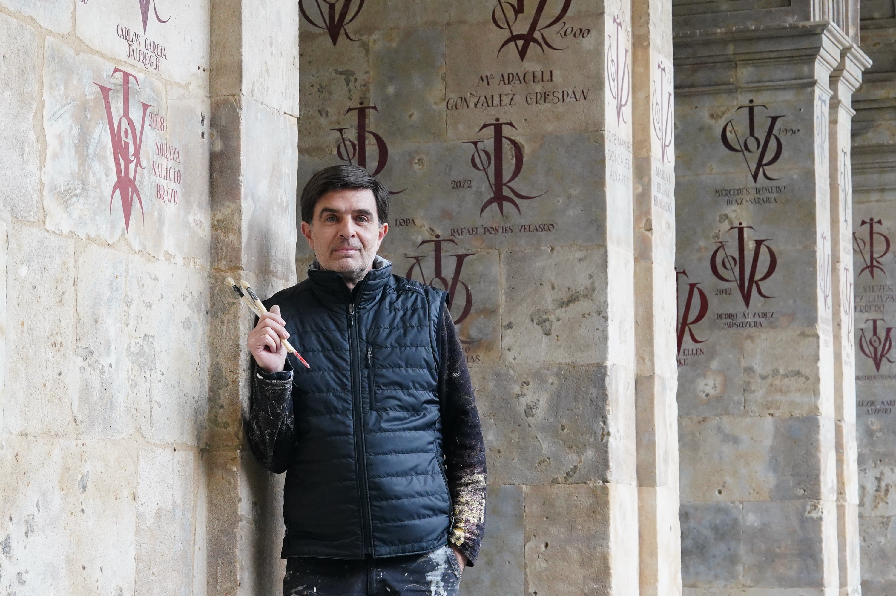 Imagen principal - Valentín Gómez, pintor y restaurador de vítores, posa en la Facultad de Filología de la Universidad de Salamanca.