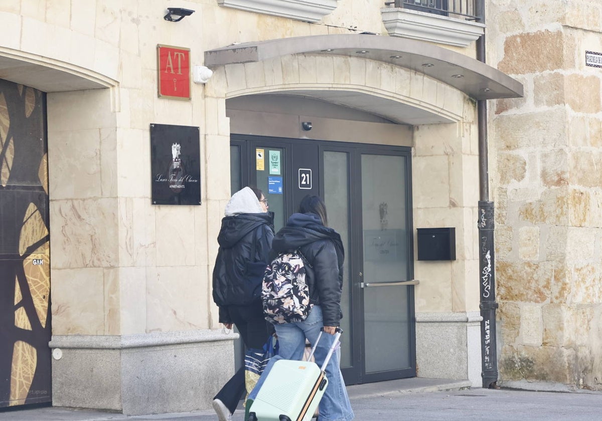 Dos jóvenes con maletas pasan frente a un alojamiento turístico.