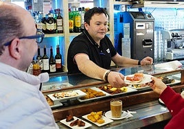 Un hostelero de un restaurante del barrio de San José ofrece un pincho a un cliente.
