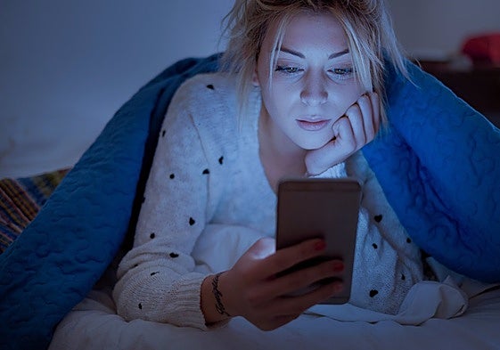 Mujer mirando el móvil por la noche en la cama.