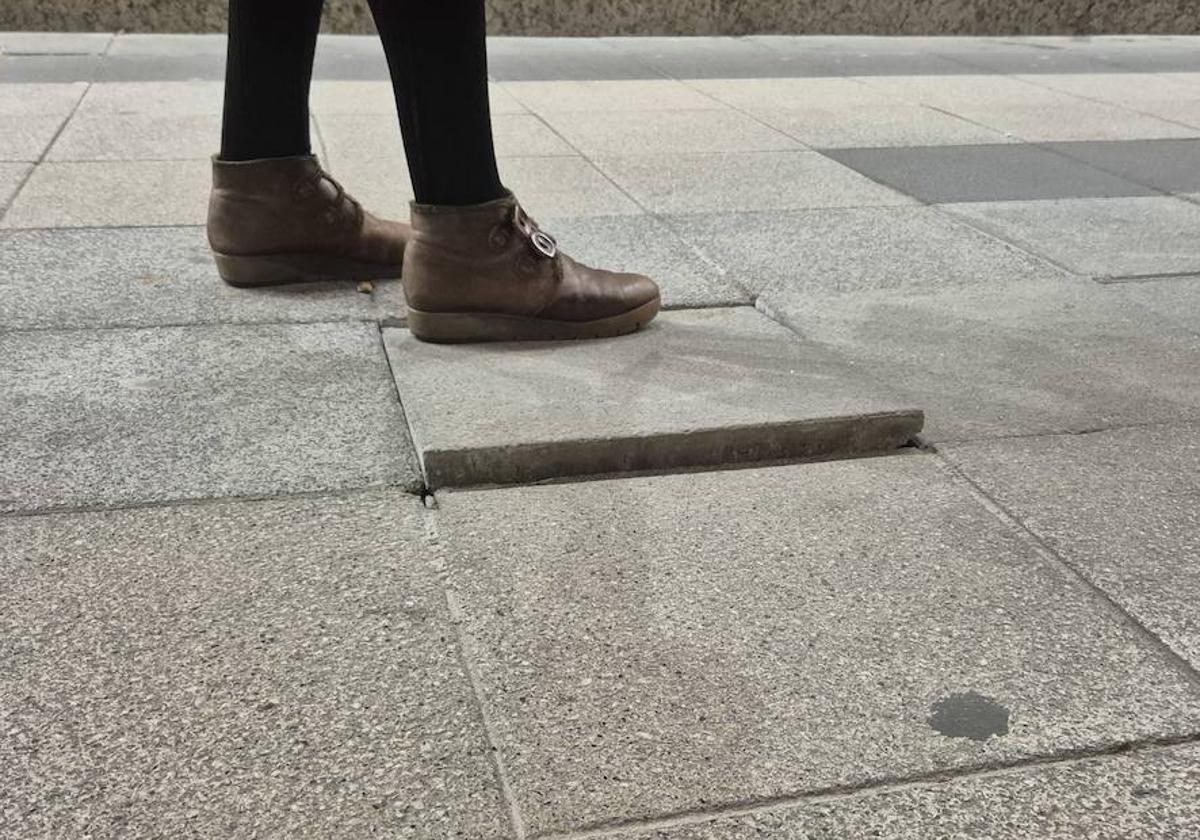 Una mujer pisa sobre una baldosa que está suelta en la vía pública.