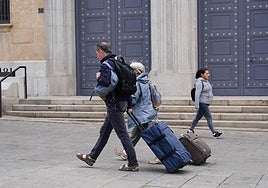 Dos personas caminan con sus maletas por la plaza de los Bandos.