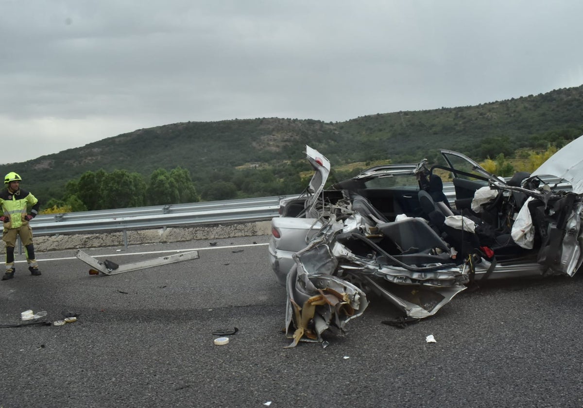 Un bombero junto al turismo accidentado, que ha quedado completamente destrozado.
