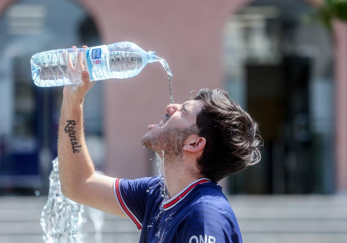 Un joven se tira una botella de agua por encima para combatir el calor.