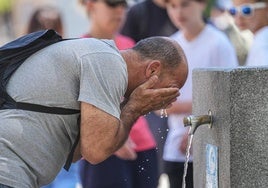 Un hombre se refresca en fuente pública.
