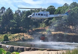 Un helicóptero carga agua en el estanque 'La Palla' para controlar el incendio en Garcibuey.