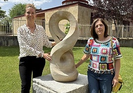 Las ediles María José García y María Soledad García con la obra 'Desarrollo evolutivo' en la zona ajardinada de la urbanización Piedra Dorada.