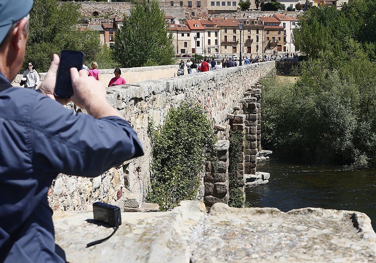 Un hombre fotografiando el muro lateral del Puente Romano, invadido por la vegetación.