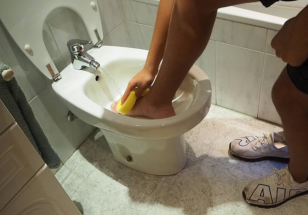 Un joven se lava los pies en el bidé de su vivienda.