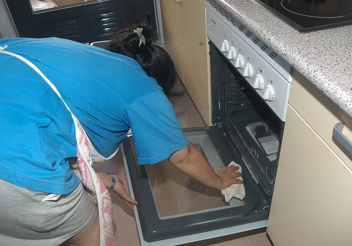 Una empleada de hogar limpia el horno de la cocina de una vivienda.