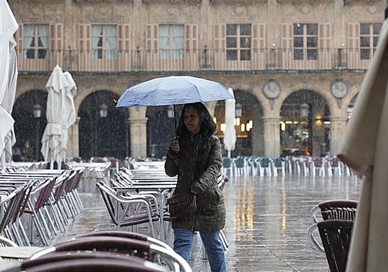 Una mujer pasa por la Plaza Mayor bajo la intensa lluvia.