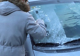 Un joven rasca un coche helado.
