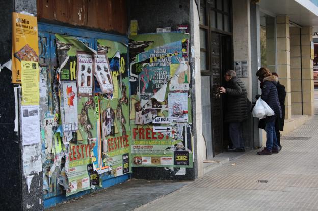 Unas personas acceden a su casa en la calle de la Vega junto a un local cerrado lleno de cartelería.