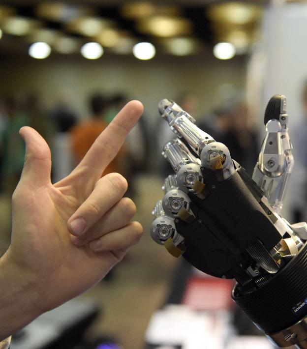 Un hombre toca la mano automatizada de un robot. :: AFP