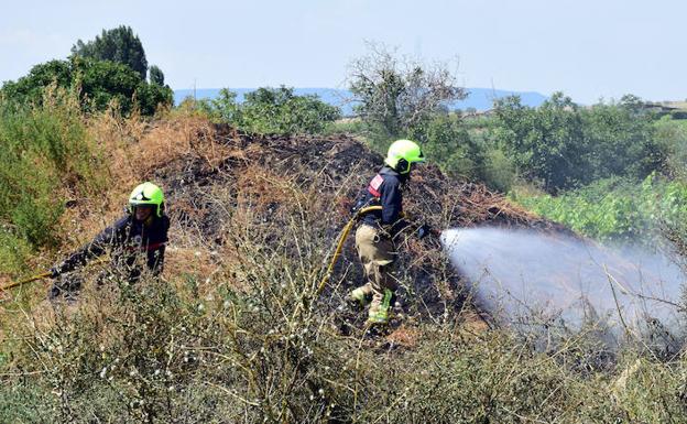 Dos bomberos proceden a remojar el terreno para evitar que vuelva a arder la maleza en el entorno de La Unión-Clavijo.