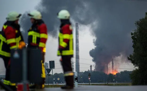 Tres bomberos ante la refinería incendiada.