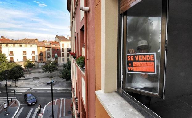 Una persona coloca un cartel de 'se vende' en una vivienda.