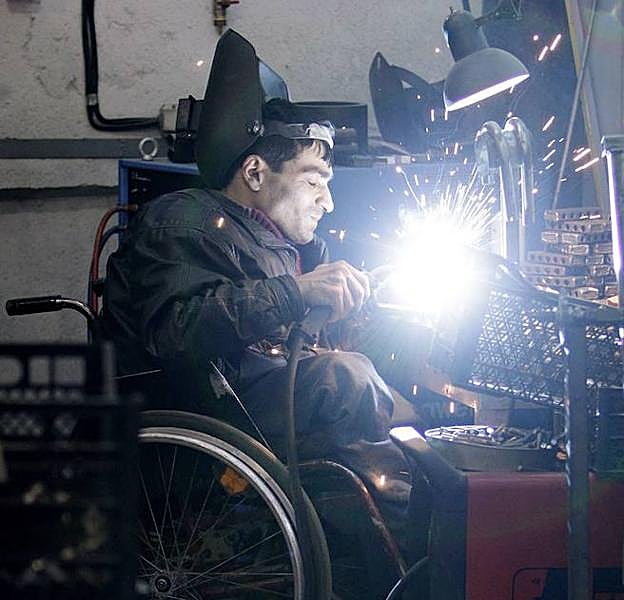 Una persona con discapacidad física trabaja en un taller de soldadura.