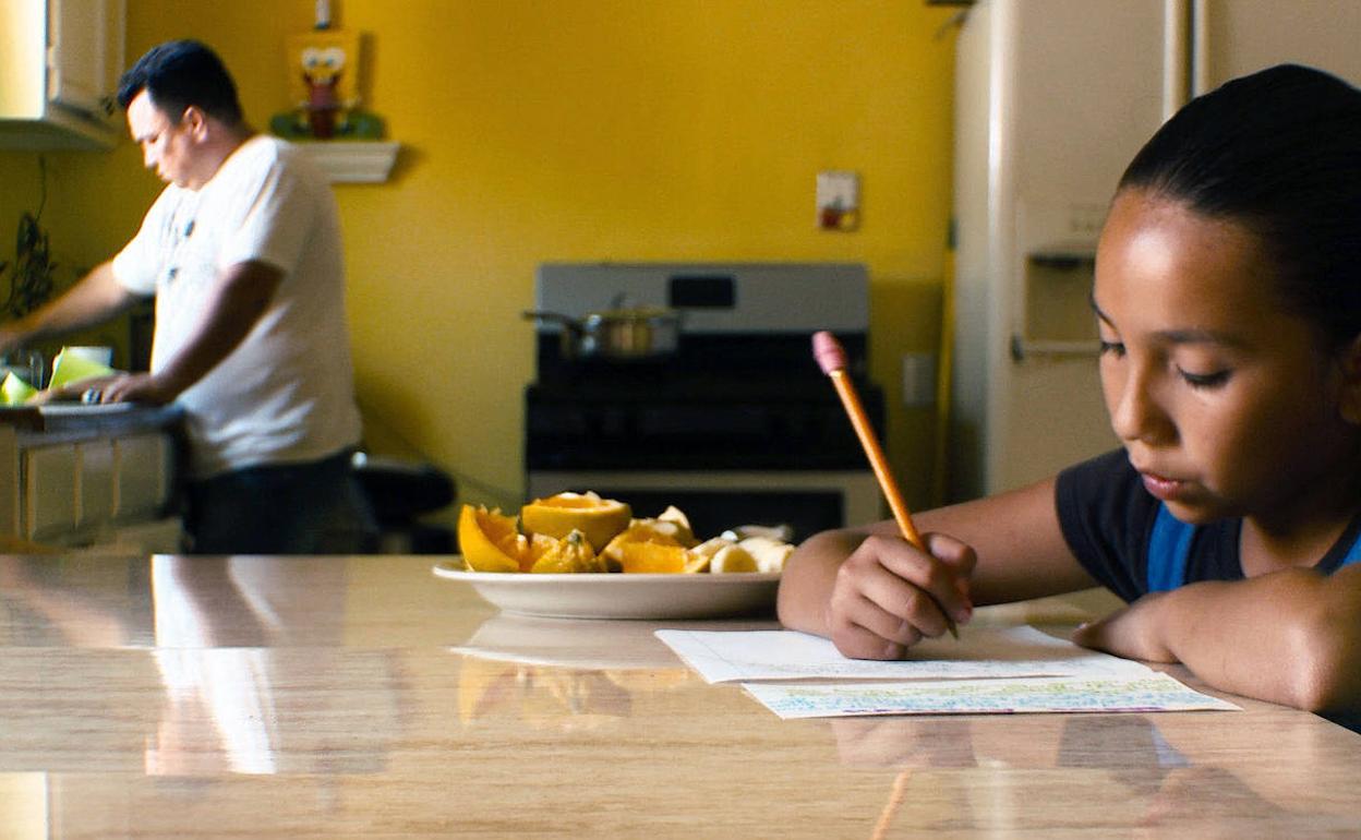 Una niña realiza sus tareas, mientras su padre cocina. 