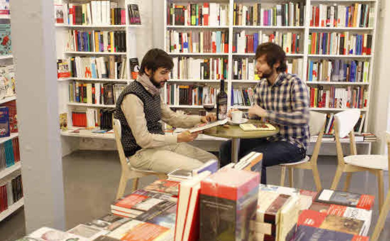 Dos clientes consultan libros y disfrutan de un vino y un café en la librería 'Tipos infames' de Madrid