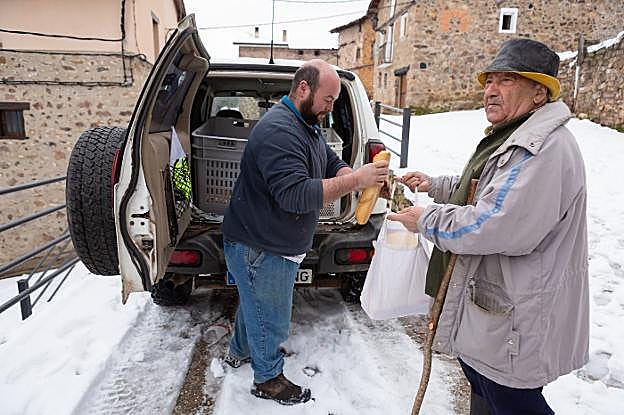 El panadero Rubén Martínez le vende unas barras a Juanjo San Pedro en Peñaloscintos, con la aldea de Ortigosa de Cameros cubierta de nieve. 