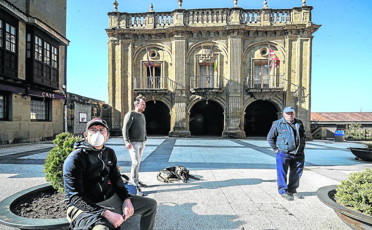 Tres vecinos de Labastida aguardan su turno en la plaza de la Paz, junto al Ayuntamiento de Labastida, para hacer la compra en la tienda de la calle Mayor.