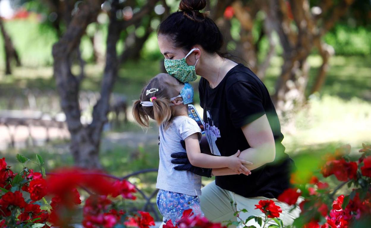 na madre y su hija, ambas protegidas con mascarillas, en un parque.