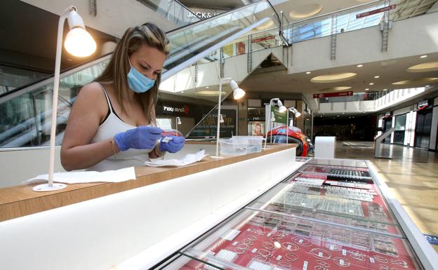 Imagen principal - Sobre esta líneas, una joven limpia una a una cada una de las piezas del muestrario de joyería expuesto en uno de los pasillos, una labor que viene desarrollando desde hace días. Abajo, las mesas de la terraza ya están preparadas para abrir siguiendo todas las normas de seguriad como recordaba ayer con un cartel un empleado.