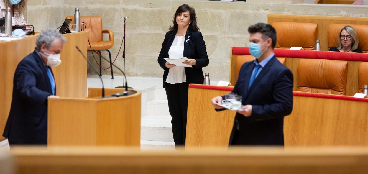 Dos trabajadores del Parlamento limpian el atril en un pleno reciente, mientras Andreu espera para intervenir. 