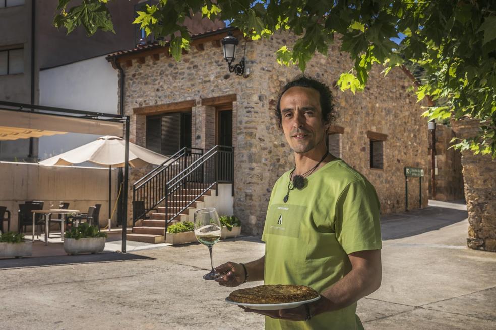 Millán Iglesias posa con su especialidad, la tortilla de patata, y un vino frente al centro social, donde regenta el bar de Leza de Río Leza. 