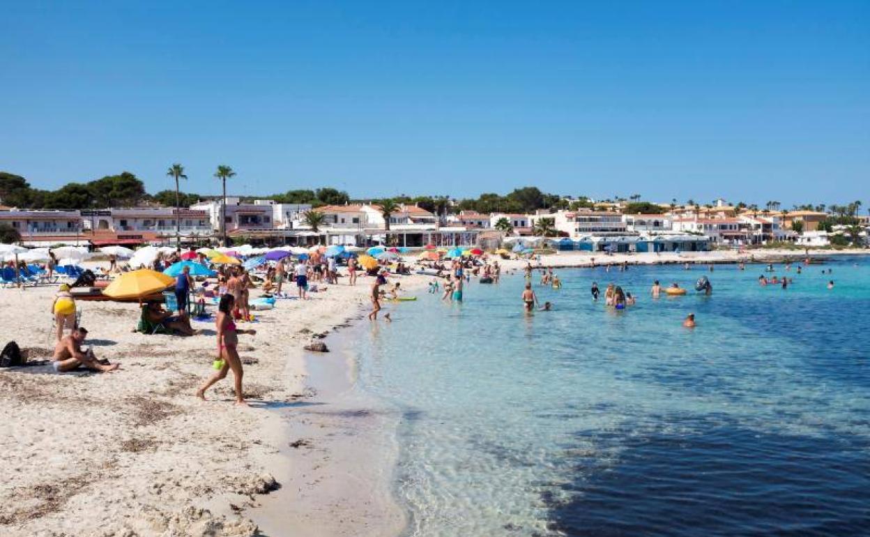 Decenas de personas disfrutan de un día soleado en una playa de Menorca.