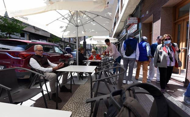 Terraza en la acera, con el aparcamiento ocupado, y camareros, clientes y paseantes compartiendo espacio. 