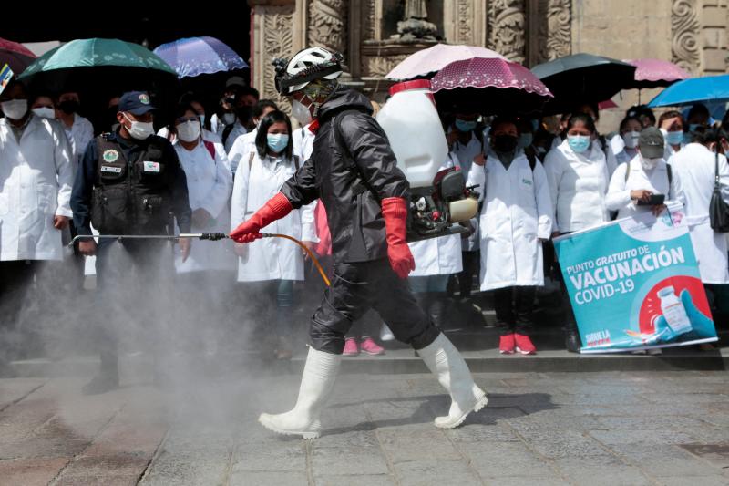 Un empleado desinfecta una calle de La Paz en Bolivia ante una manifestación de sanitarios 