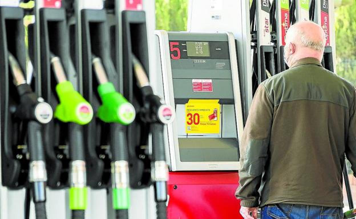 Un usuario observa el surtidor de una gasolinera mientras reposta combustible.